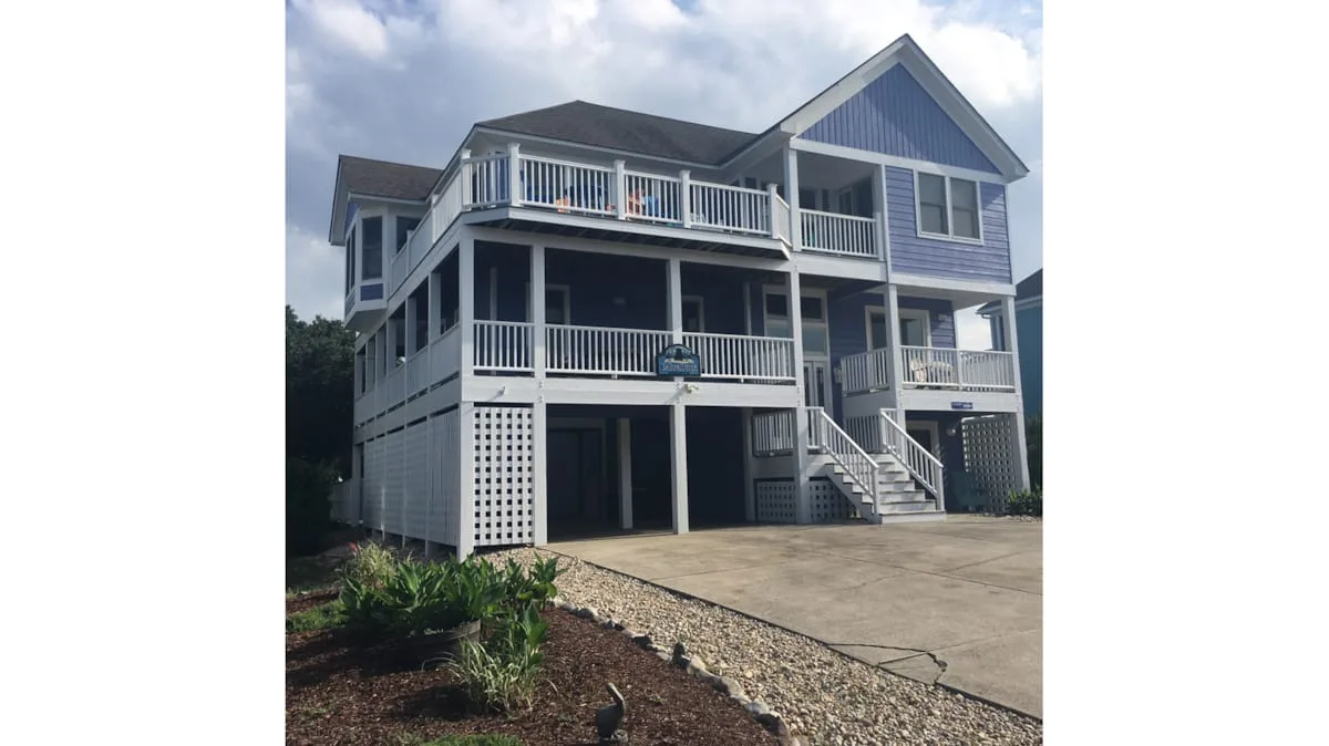 A large elevated house with wraparound balconies and a paved driveway.