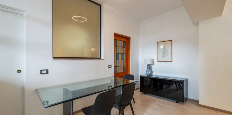 A bright dining area with a glass table and dark seating.