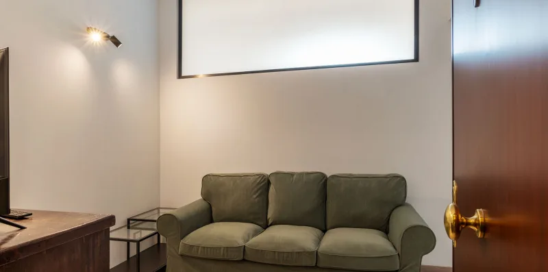 A living room with a three-seat sofa and a wall-mounted screen.