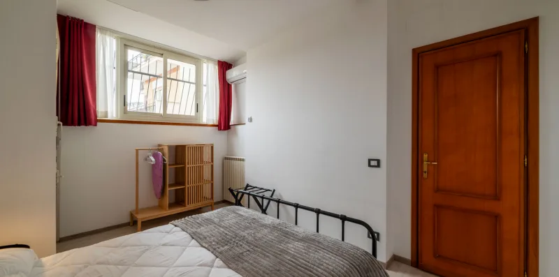 A bedroom with a bed, barred window, and wooden door.