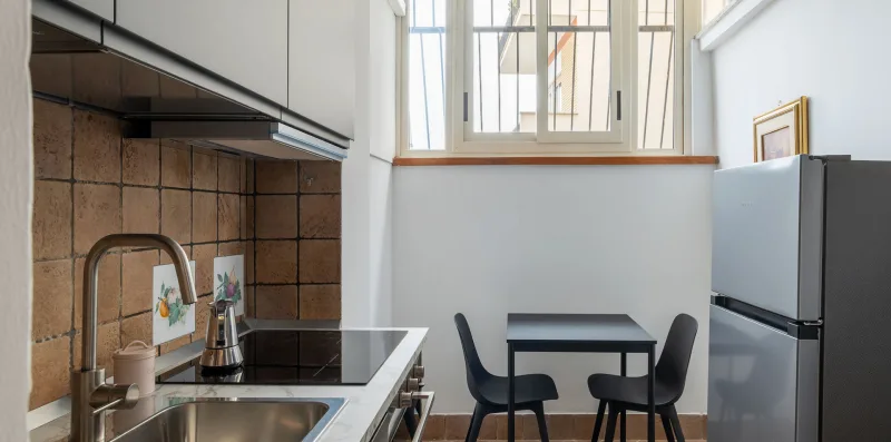 A compact kitchen with a counter, dining table, and tall windows.