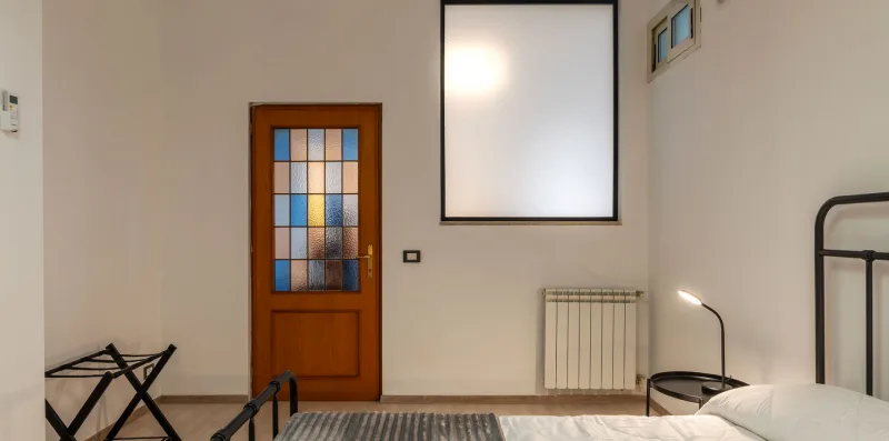 A bedroom with a bed, a stained-glass door, and a wall-mounted radiator.