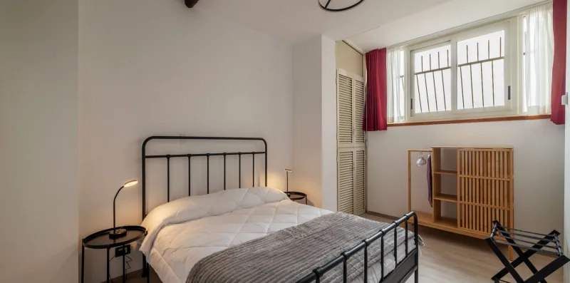 A bedroom with a bed, a high window, and a wooden cabinet.