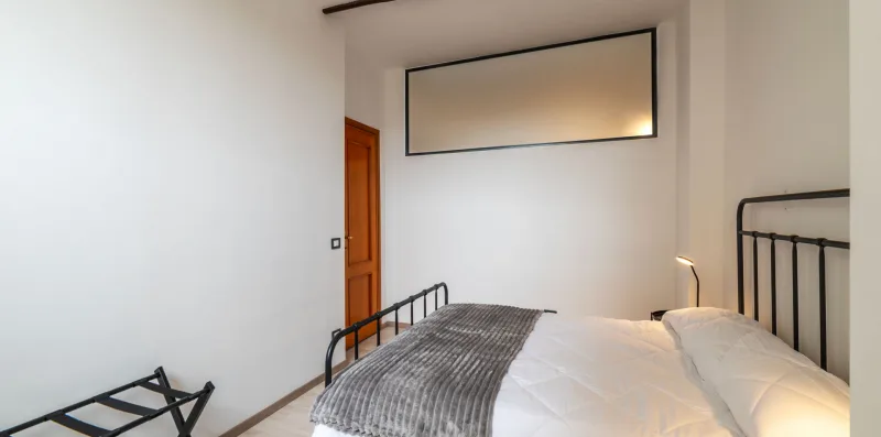 A bedroom with a bed, gray blanket, and black metal headboard.