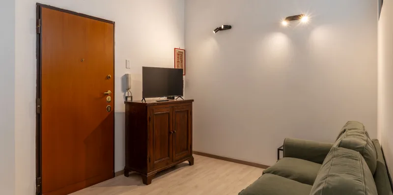 Una sala de estar con un sofá verde y un mueble de madera junto a la puerta de entrada.