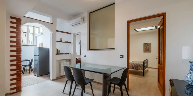 A dining area with a glass table and seating beside an arched kitchen opening.