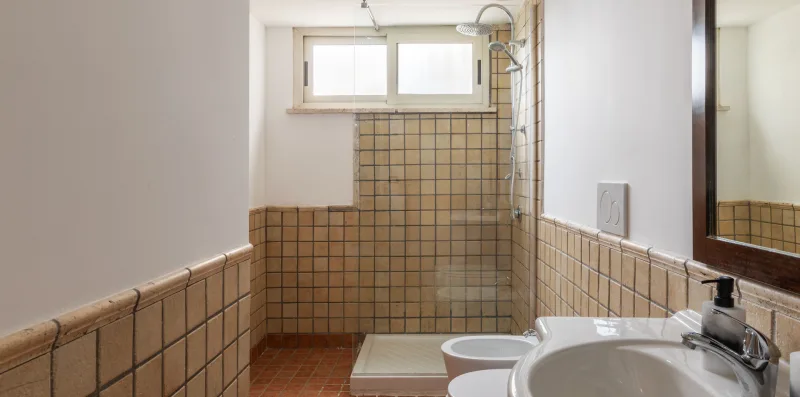 A tiled bathroom with a shower, toilet, and sink beneath a small window.