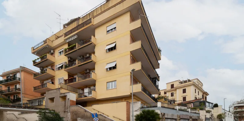 A multi-story apartment building with balconies stands along a street.