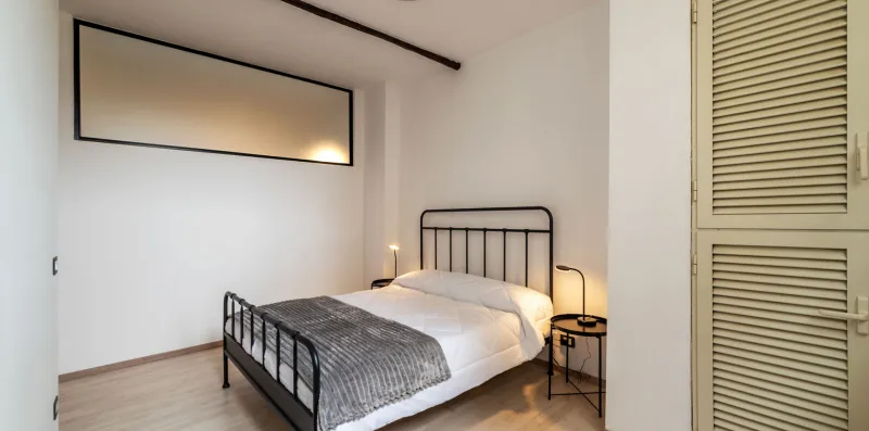 Un dormitorio con una cama, mesas de noche y una puerta de armario con persianas.