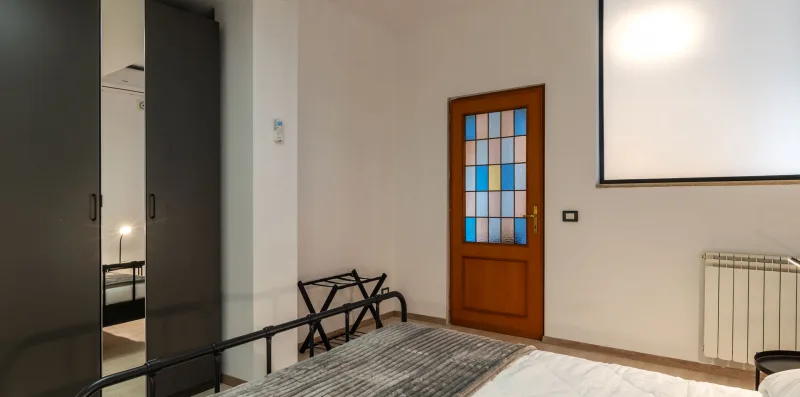 A bedroom with a bed, dark wardrobes, and a wooden door with colored glass.