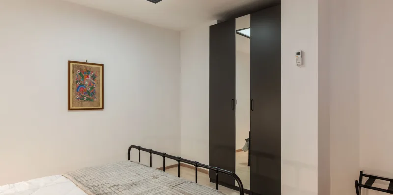 A bedroom with a bed, framed artwork, and a dark wardrobe.