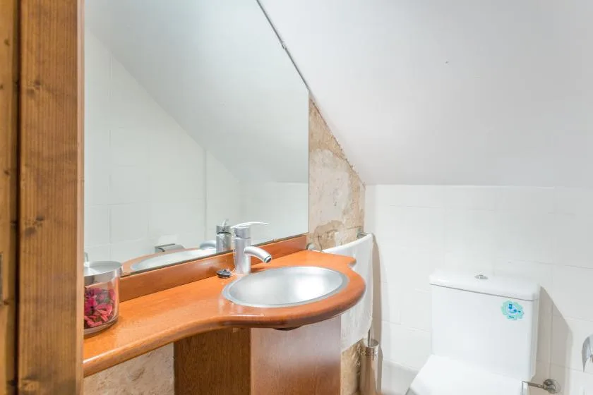 A bathroom vanity with a round basin and a toilet beneath a sloped ceiling.