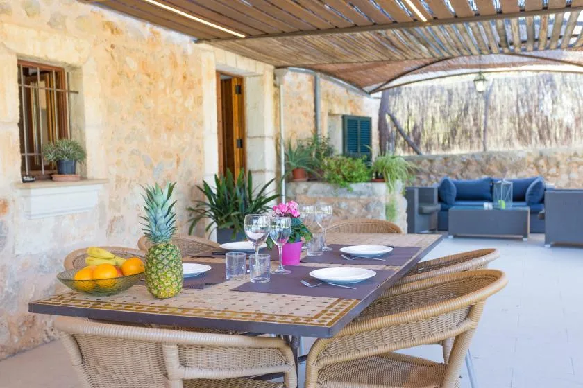 A covered outdoor dining area with a table and lounge seating.