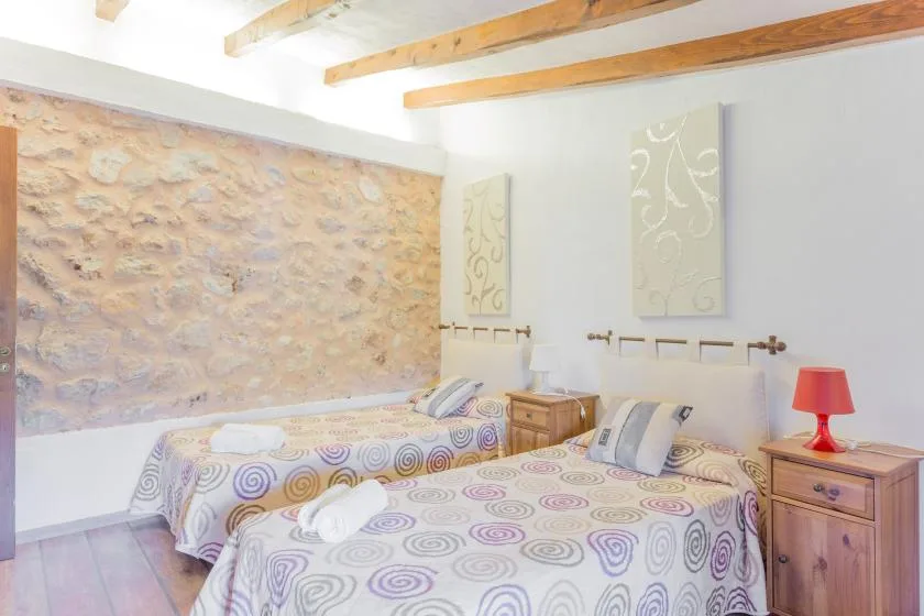 A bedroom with two beds, patterned bedding, and wooden ceiling beams.