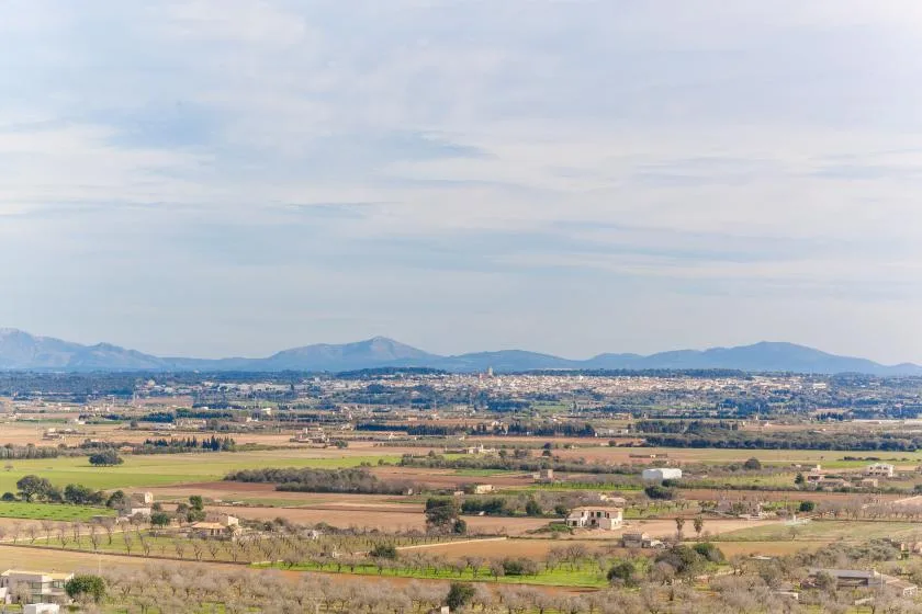 A broad rural landscape with fields, scattered buildings, and distant hills beneath a cloudy sky.