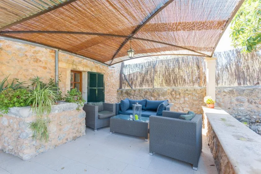 A covered outdoor seating area with cushioned seating beside a stone wall.