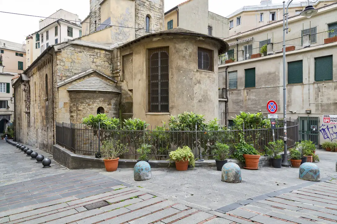 Una iglesia de piedra junto a una plaza pavimentada con plantas en macetas y barandillas metálicas.