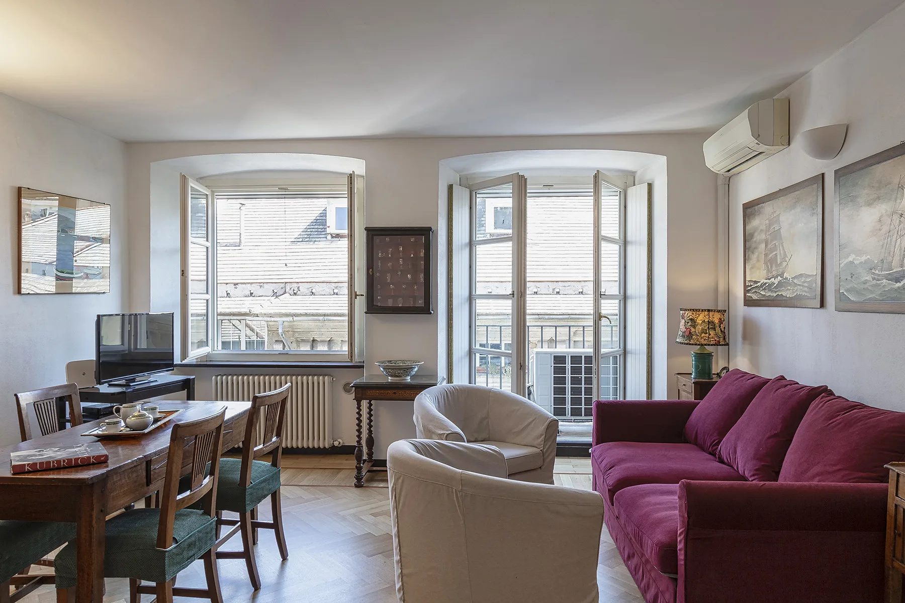 Una sala de estar y comedor con asientos, una mesa y ventanas altas.
