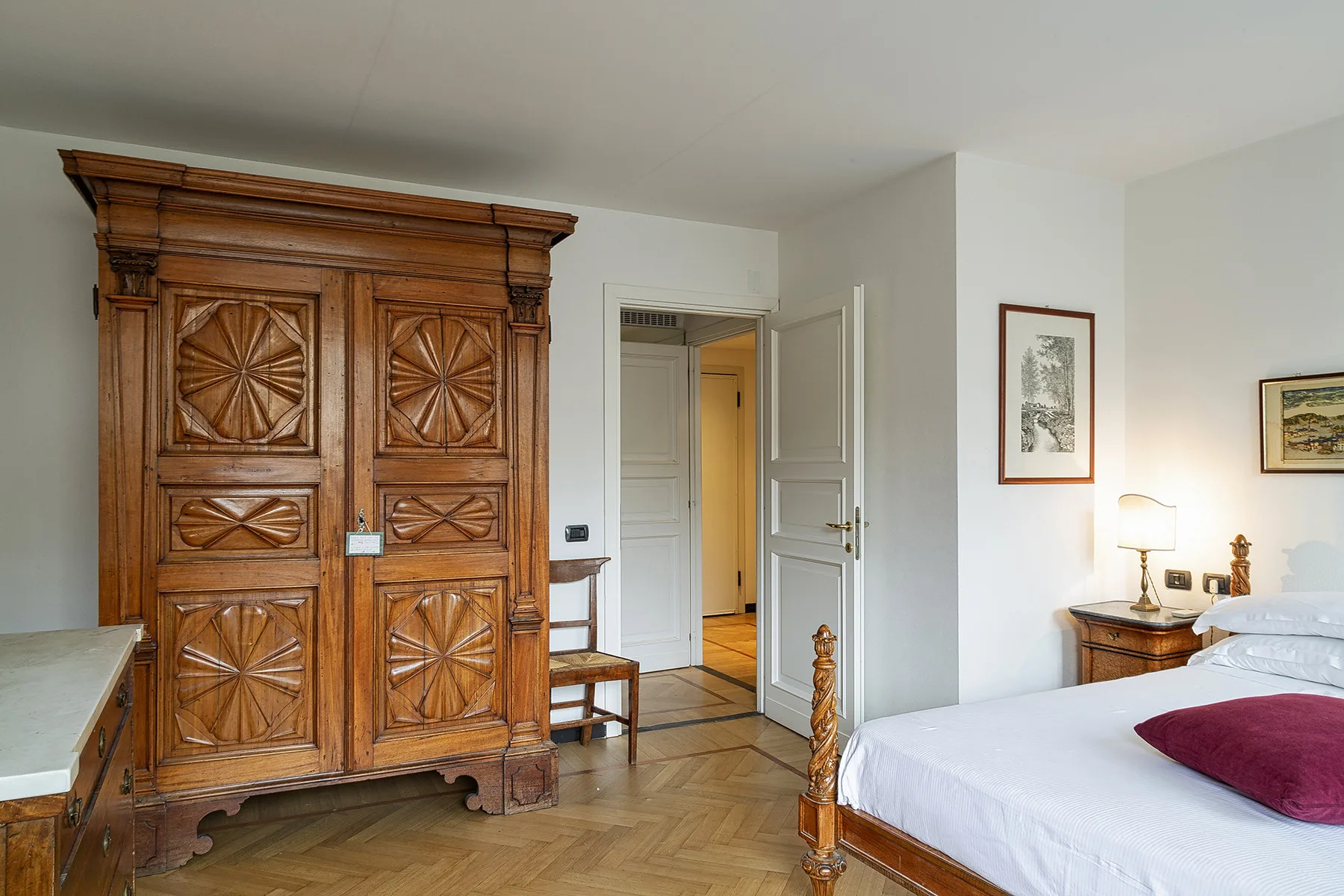 Un dormitorio con un armario de madera tallada, una cama y una puerta abierta.