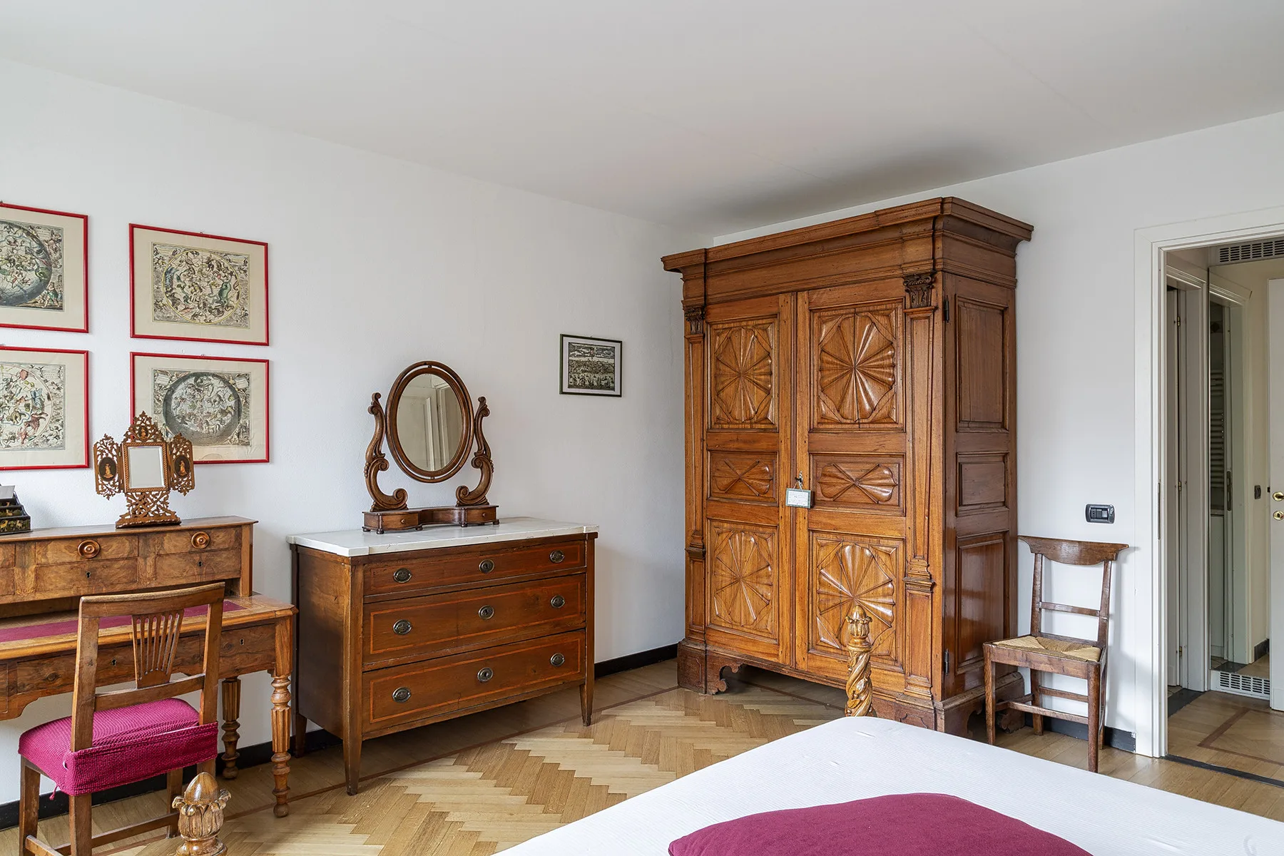 Un dormitorio con muebles de madera tallada, cuadros enmarcados y una cama en primer plano.