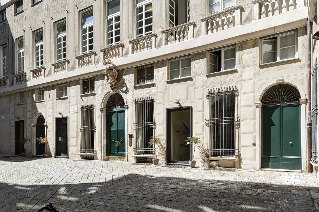 Fachada de piedra con puertas verdes y ventanas enrejadas junto a una calle pavimentada.