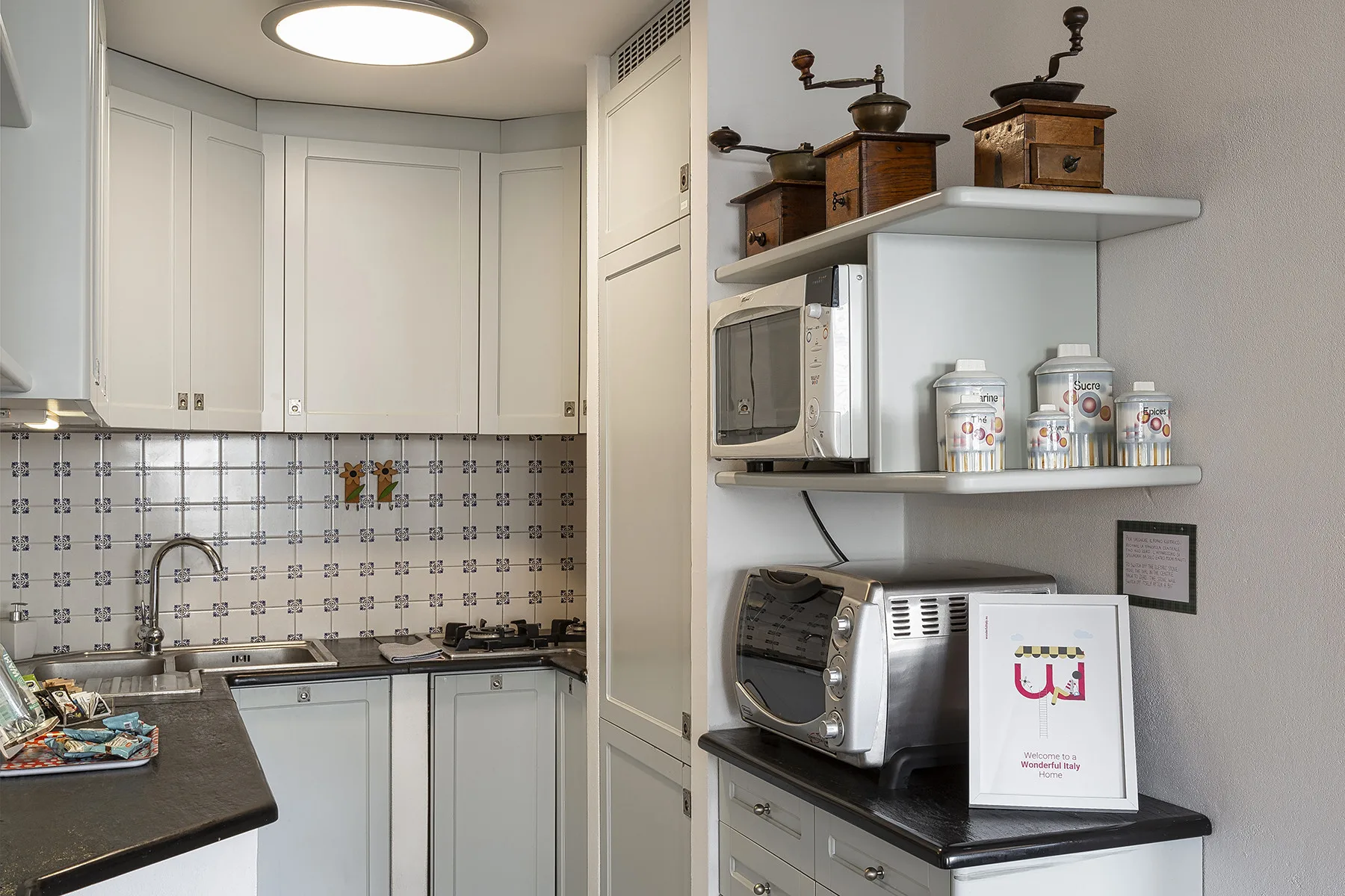 Una cocina pequeña con gabinetes blancos, un salpicadero estampado y electrodomésticos sobre la encimera.