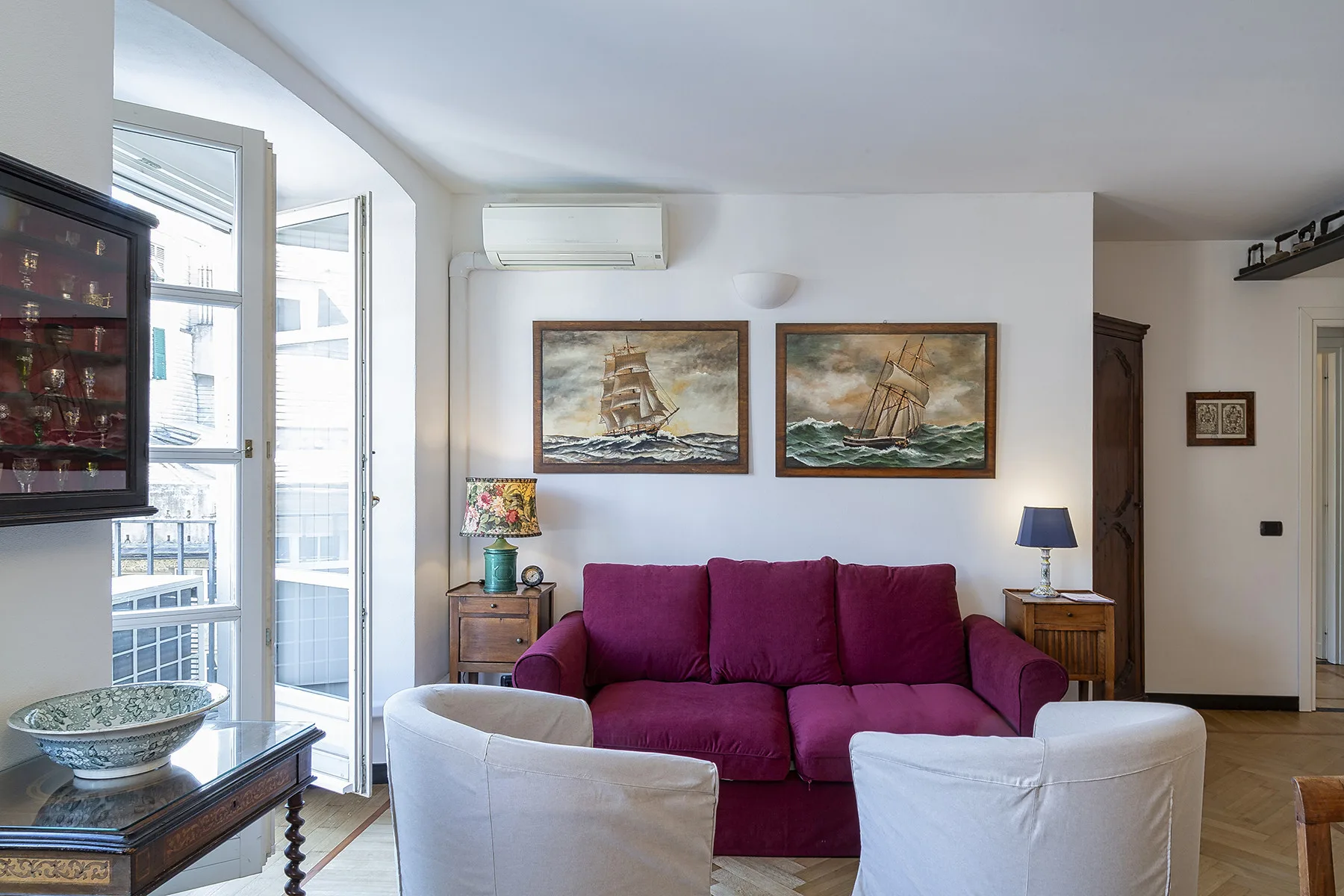 Una sala de estar con asientos magenta, dos sillones blancos y cuadros enmarcados de barcos.