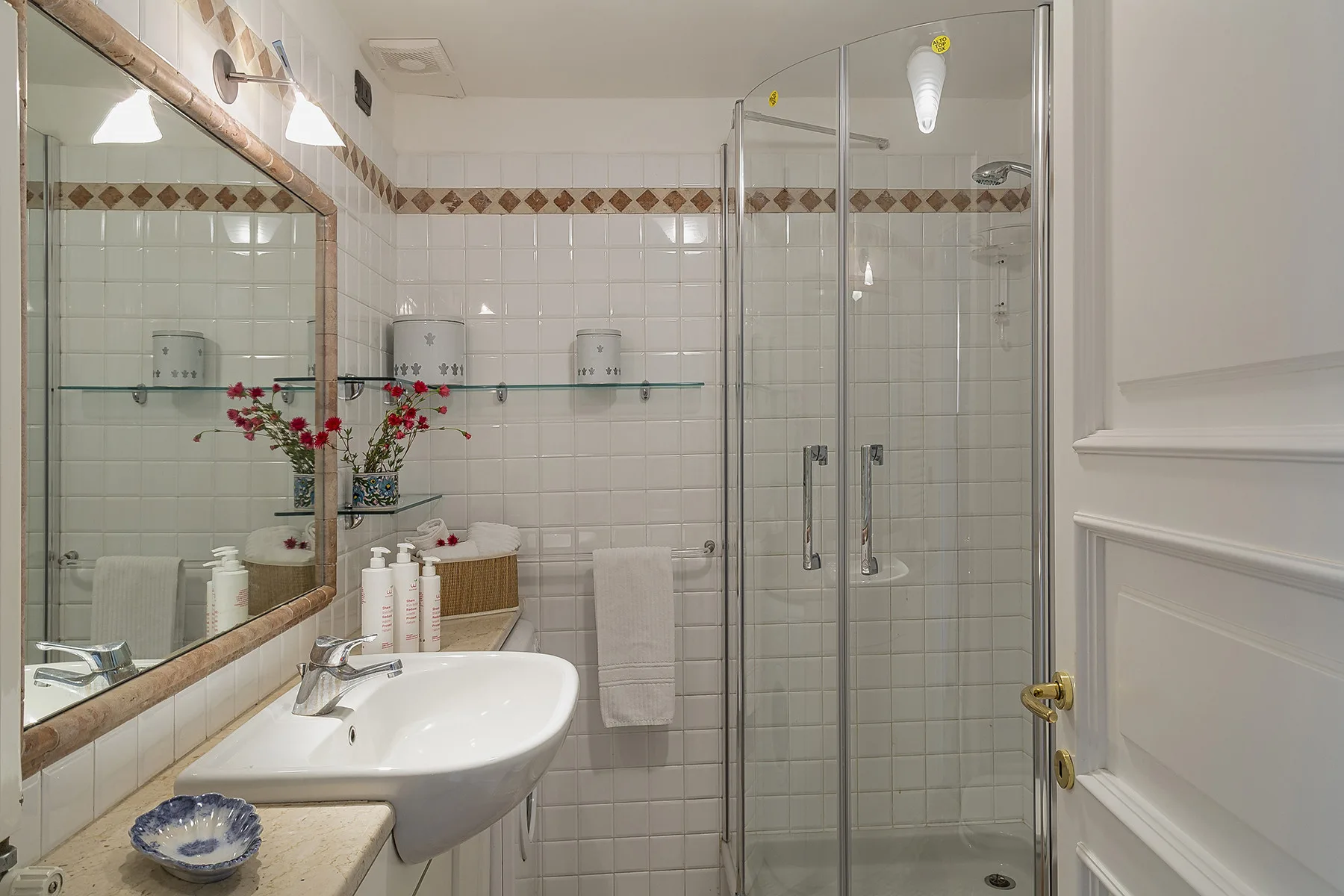 Un baño alicatado con ducha de vidrio, lavabo y espejo de pared.