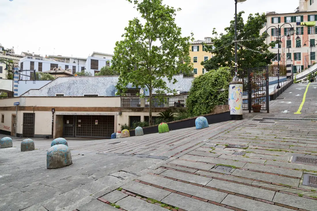 Una plaza pavimentada al aire libre desciende hacia una calle bordeada de edificios y árboles.