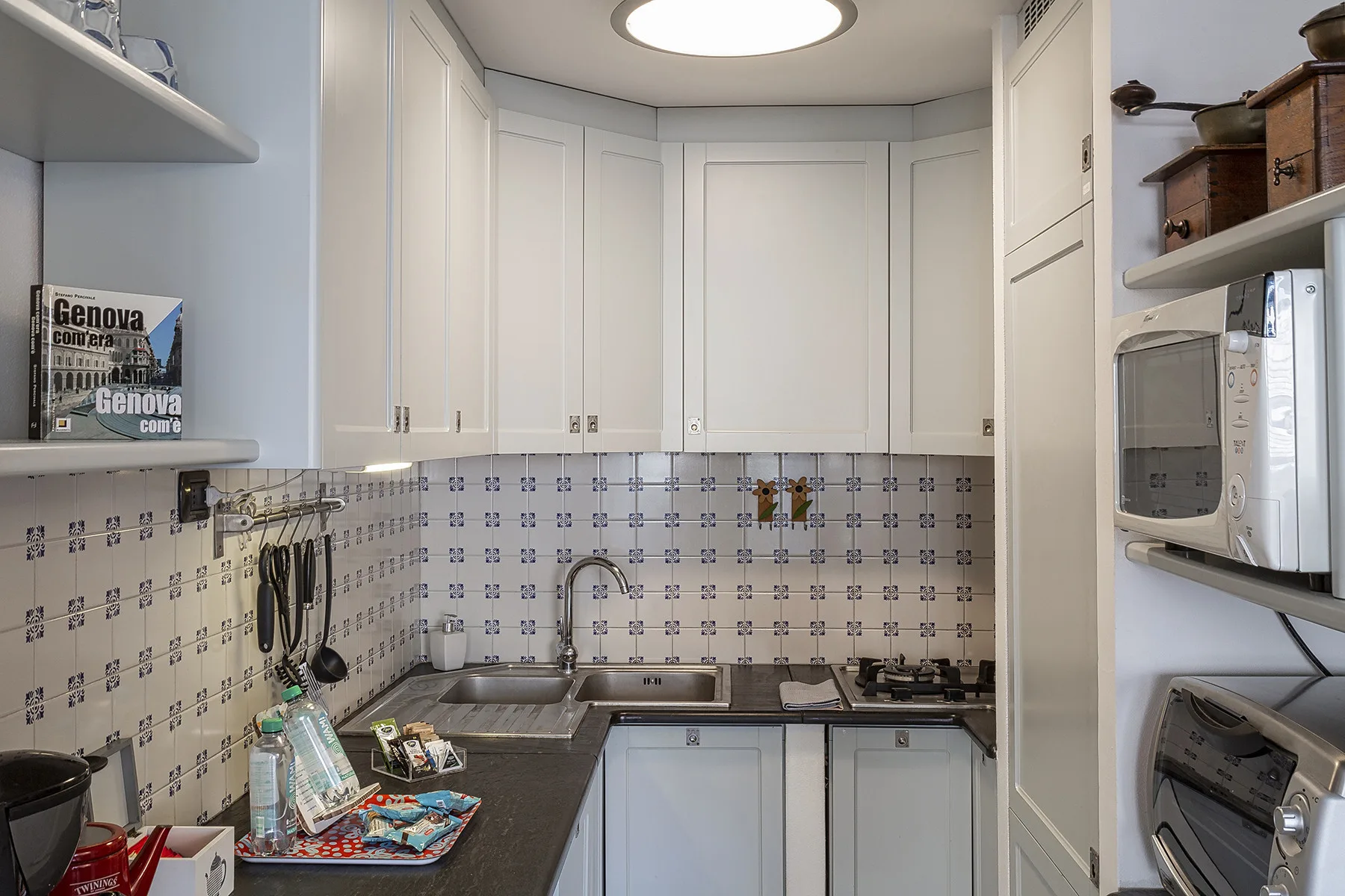 Una cocina compacta con gabinetes blancos, paredes de azulejos y un fregadero en la encimera.