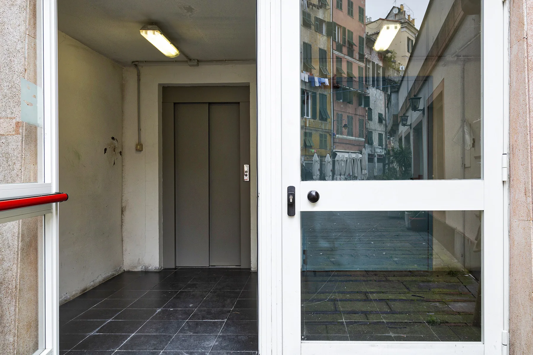 Entrada de un edificio con puerta de vidrio y un pequeño vestíbulo con suelo de baldosas.