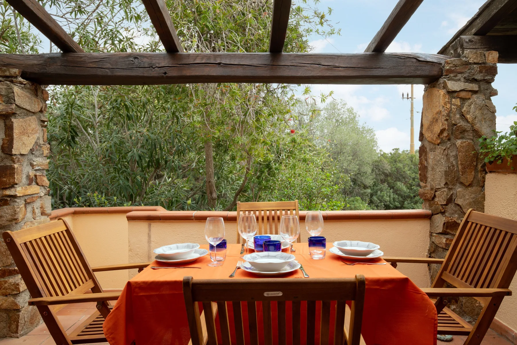 Un comedor al aire libre con una mesa puesta bajo una pérgola de madera.