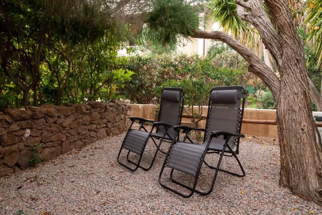 Un patio de grava con asientos reclinables bajo un árbol grande.
