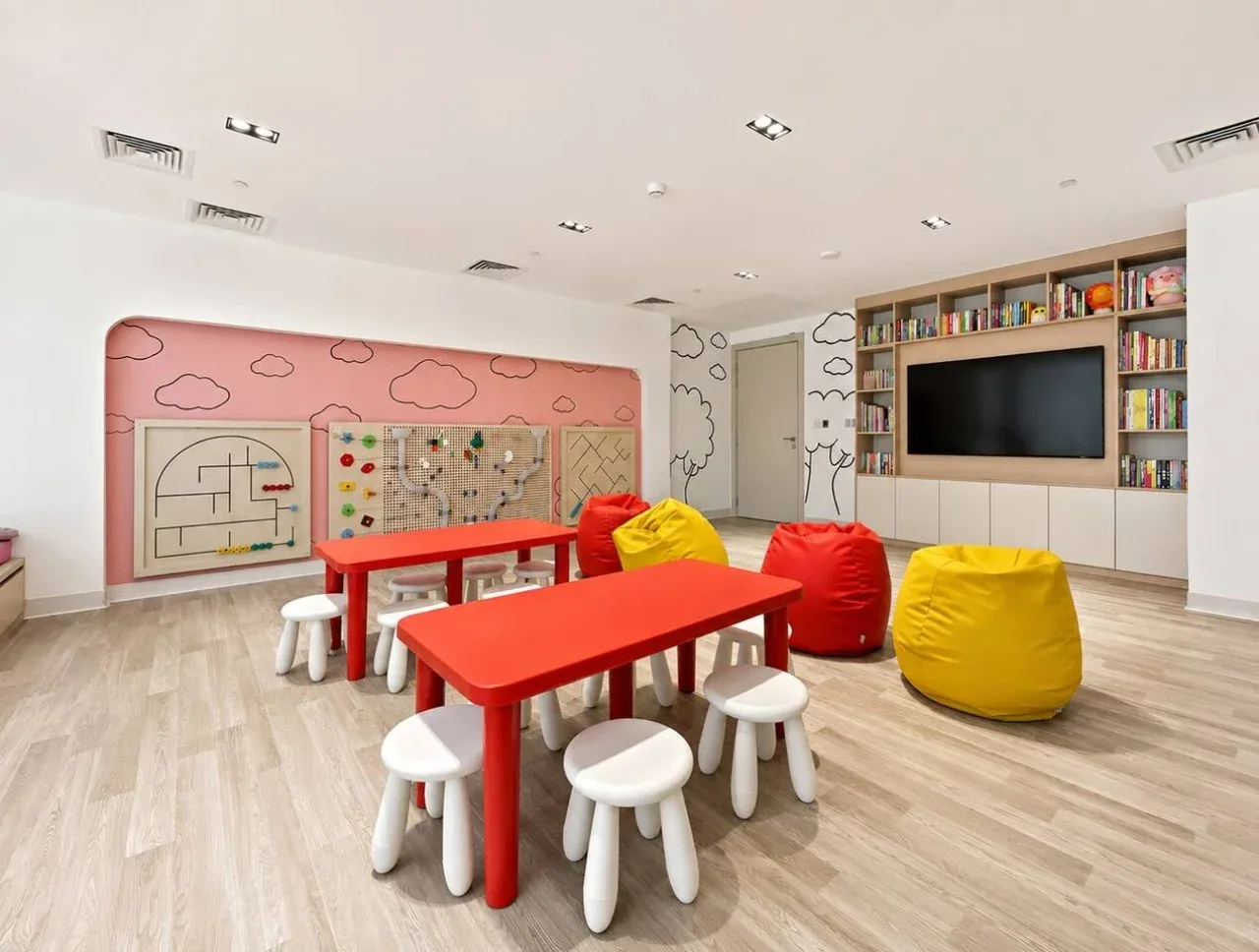A colorful playroom with low red tables, small stools, and beanbag seating.