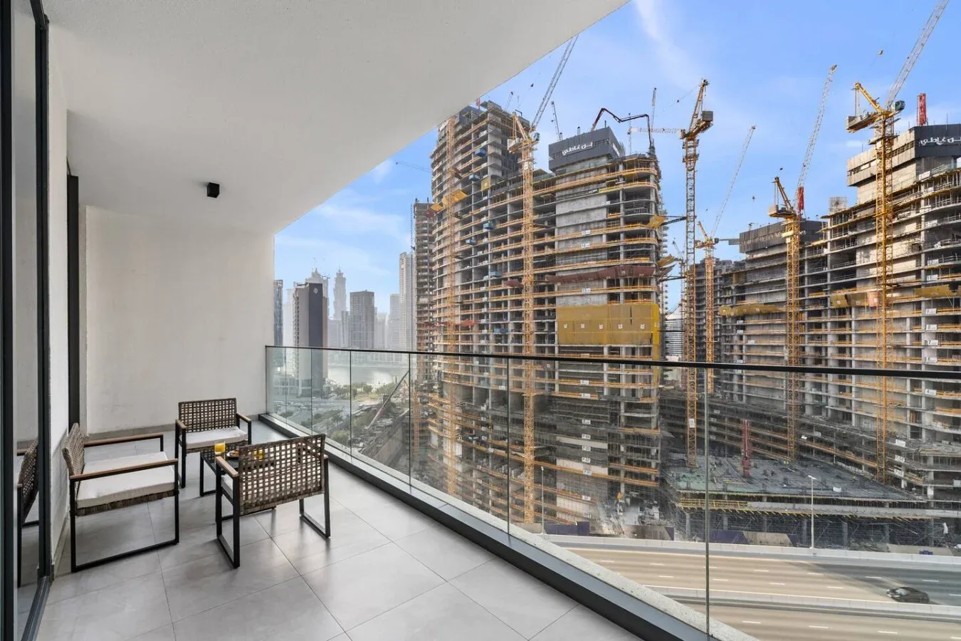 A balcony with seating overlooks nearby high-rise construction and cranes.
