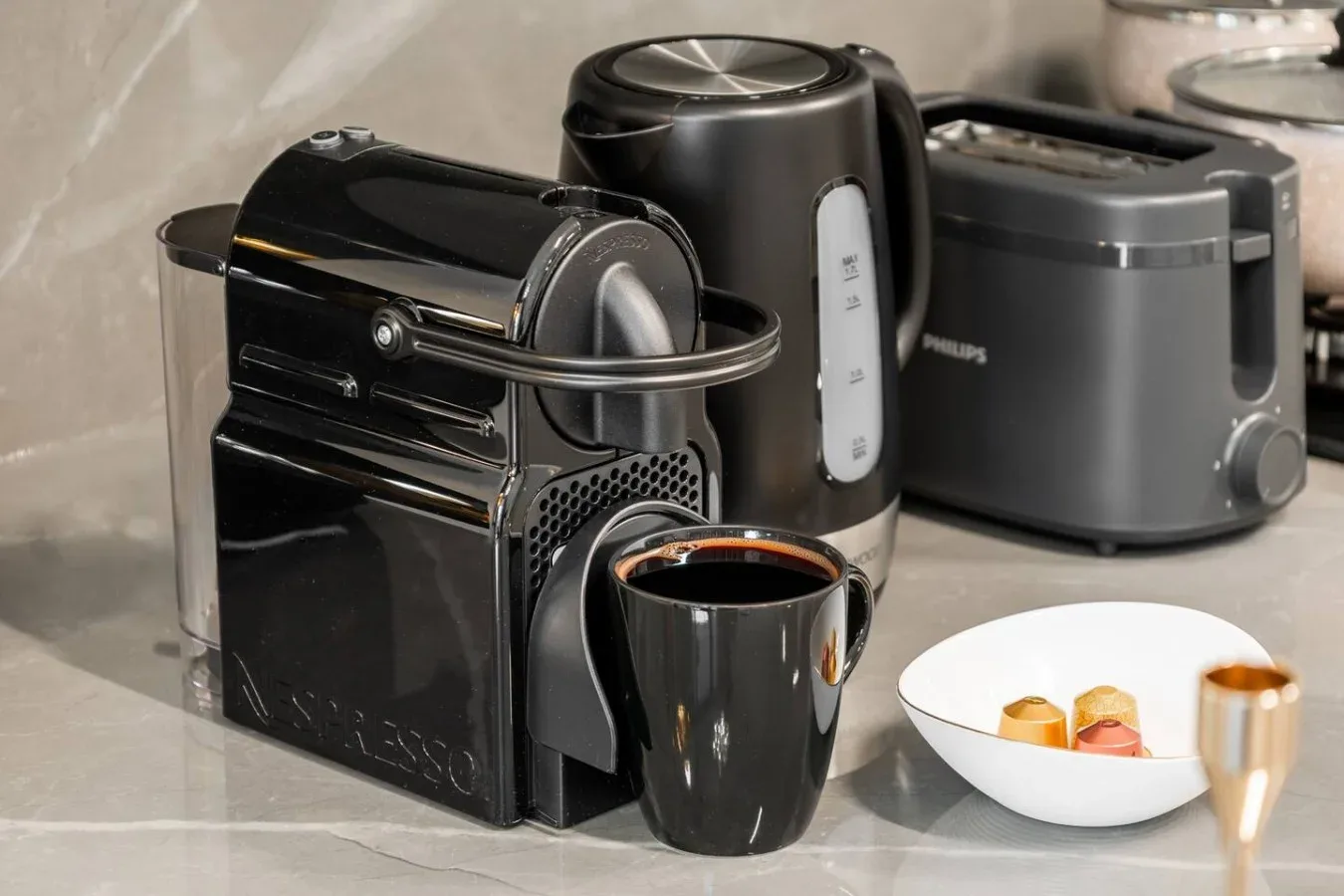 A kitchen counter displays a coffee machine, kettle, toaster, and cup.