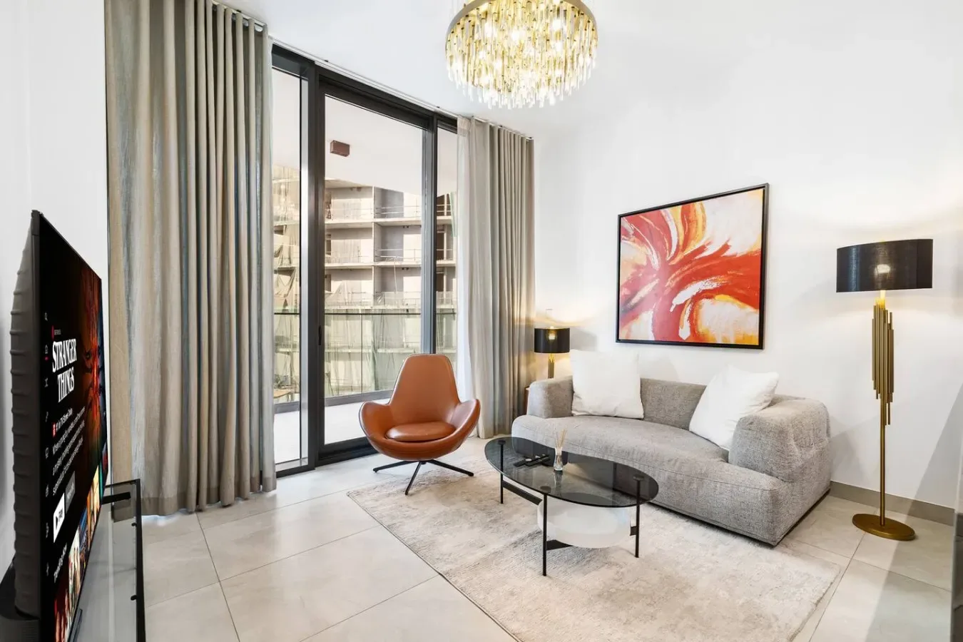 Una sala luminosa con sofá gris, mesa de centro de vidrio y ventanas altas.