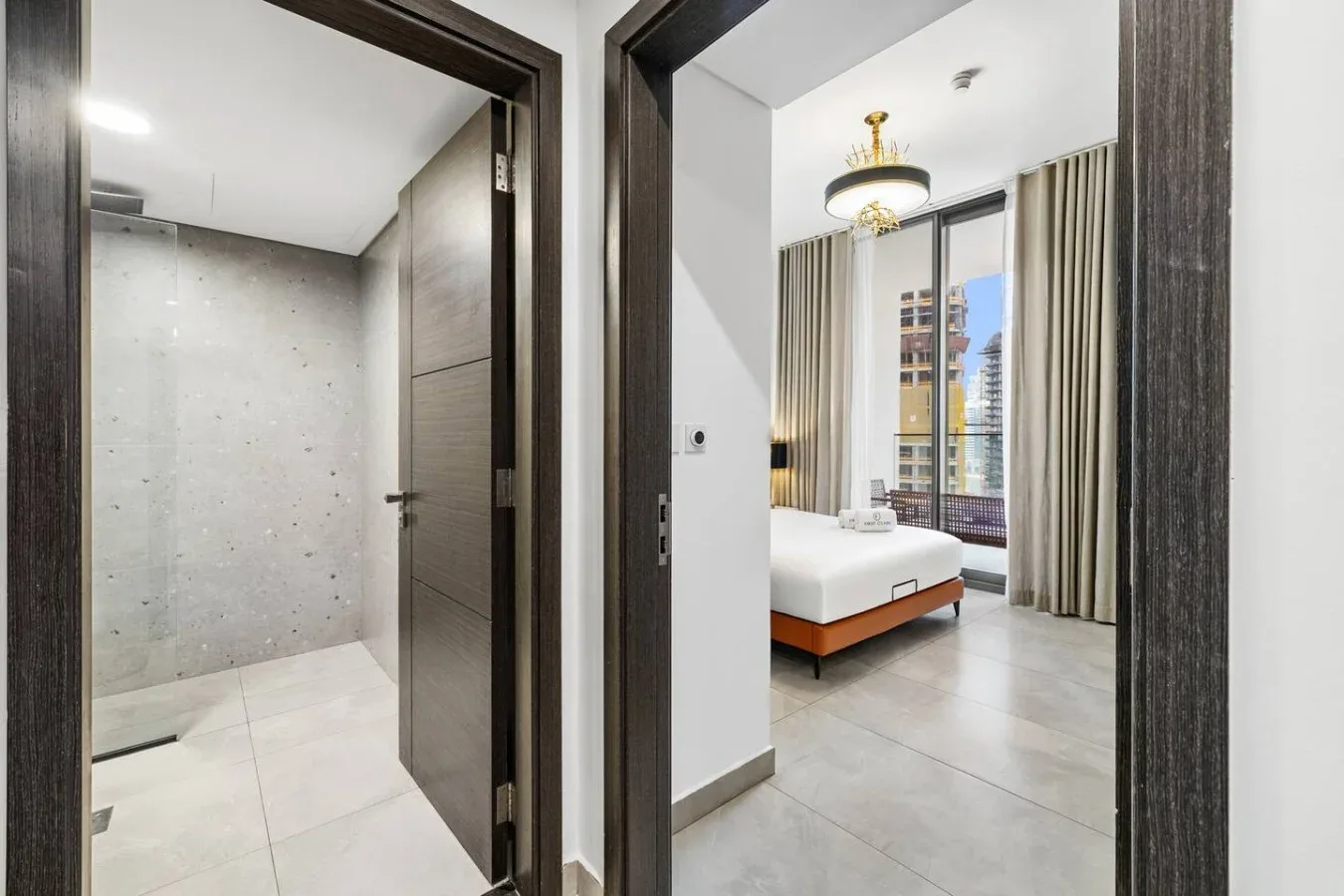 A bedroom with a bed beside tall curtained windows, viewed through an open doorway.