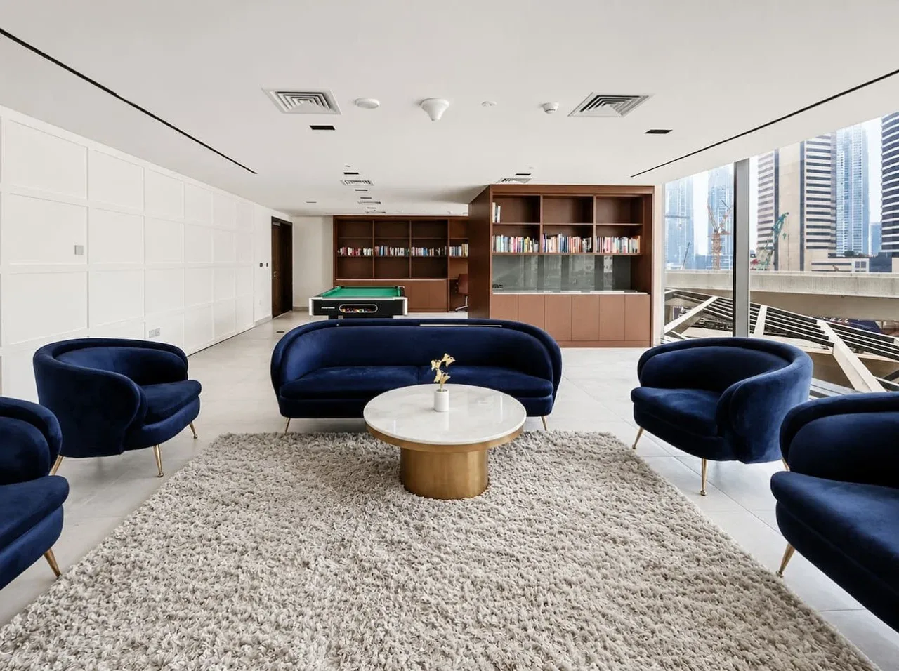 A modern lounge with blue seating, a round coffee table, and large windows.