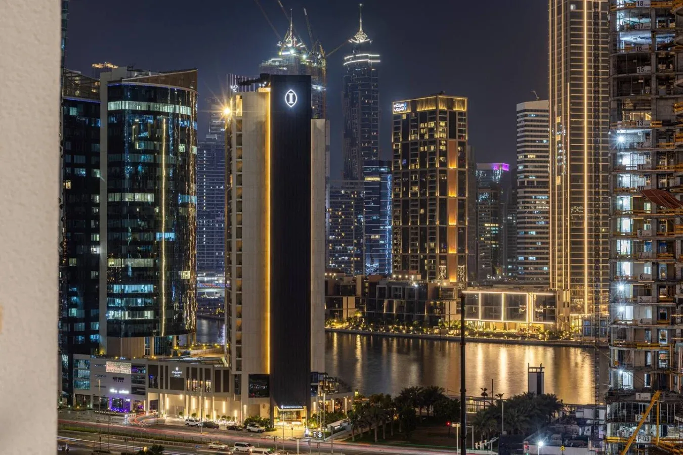 A nighttime city skyline with illuminated high-rise buildings beside the water.