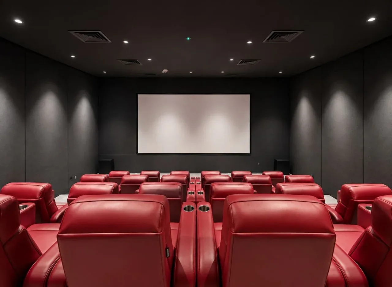 A private screening room with rows of red reclining seats facing a large projection screen.