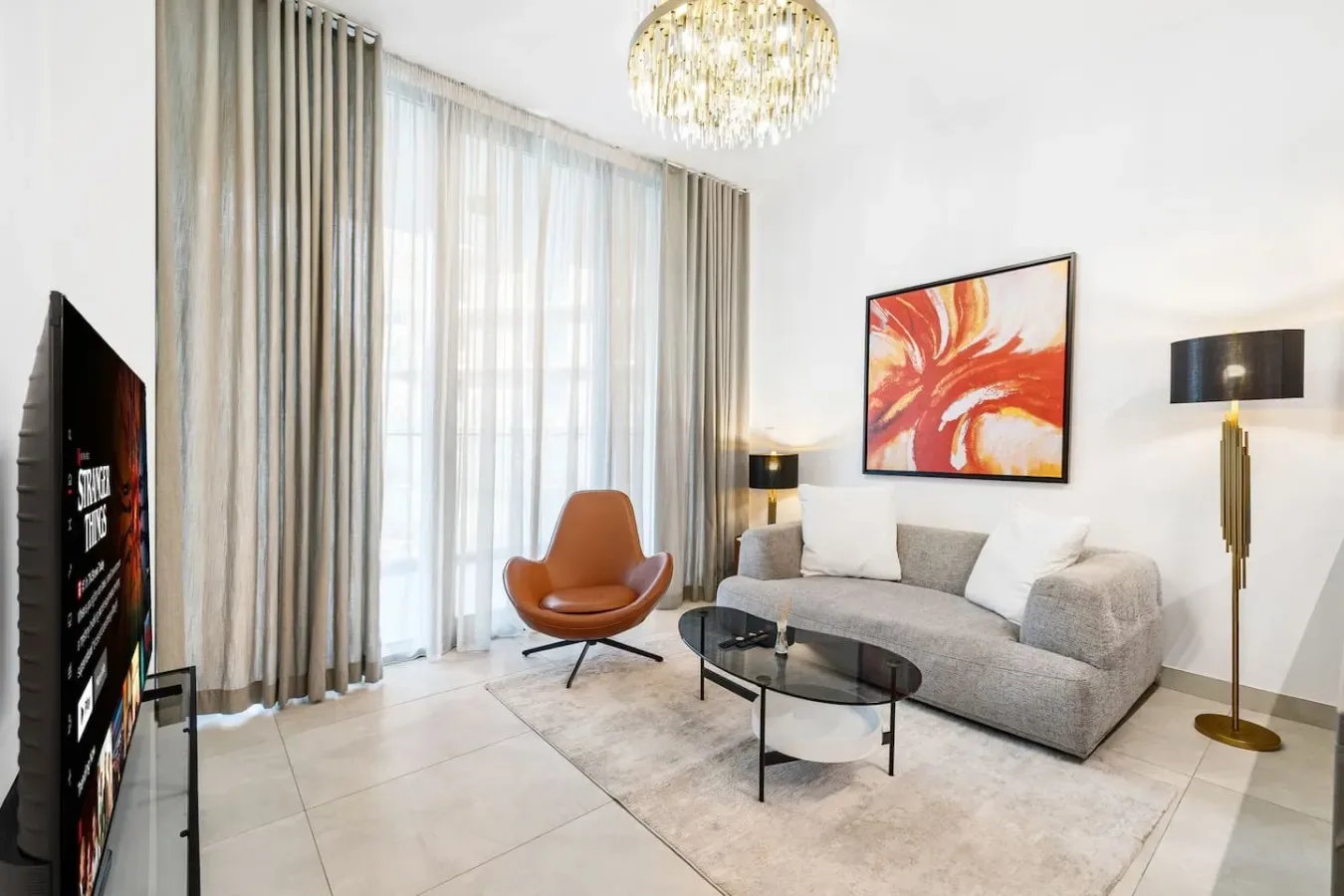 Una sala luminosa con sofá, mesa de centro de vidrio y grandes ventanas con cortinas.