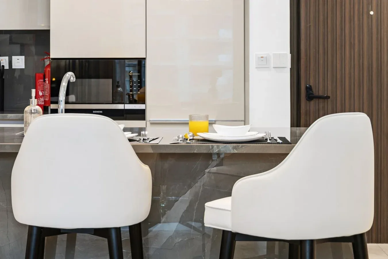A dining table with white seating is set in front of a kitchen counter.