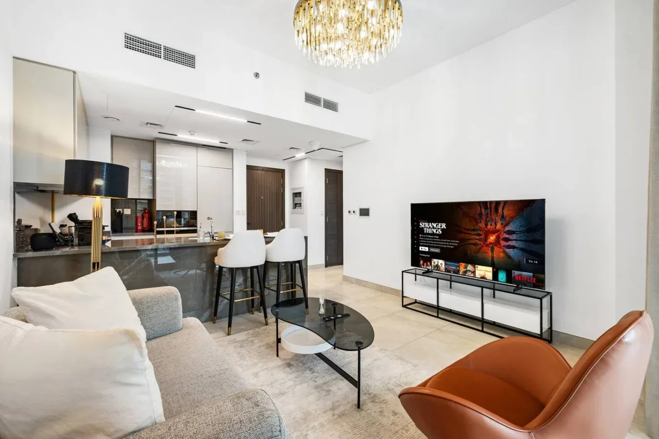 A bright open-plan living room features a television and a kitchen bar.