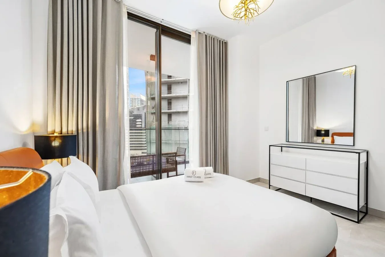A bright bedroom with a white bed and tall curtained windows.
