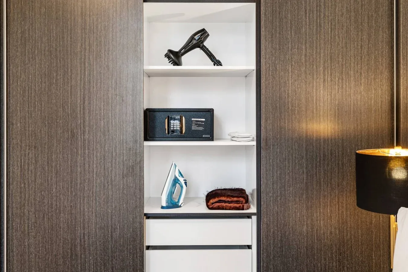 A built-in shelving unit holds a hair dryer, an electronic safe, and folded towels.