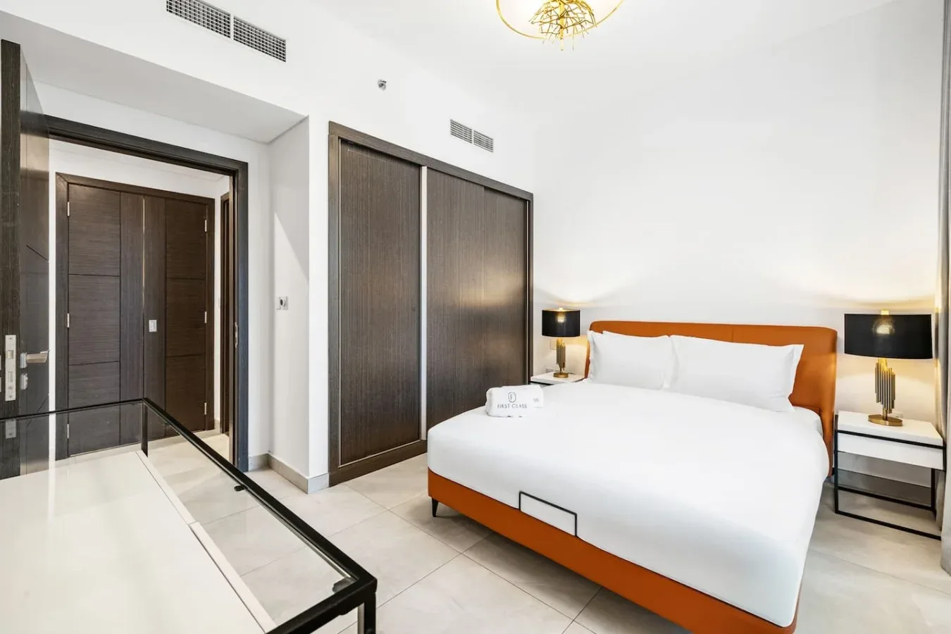 A bright bedroom with a neatly made bed and dark built-in wardrobes.