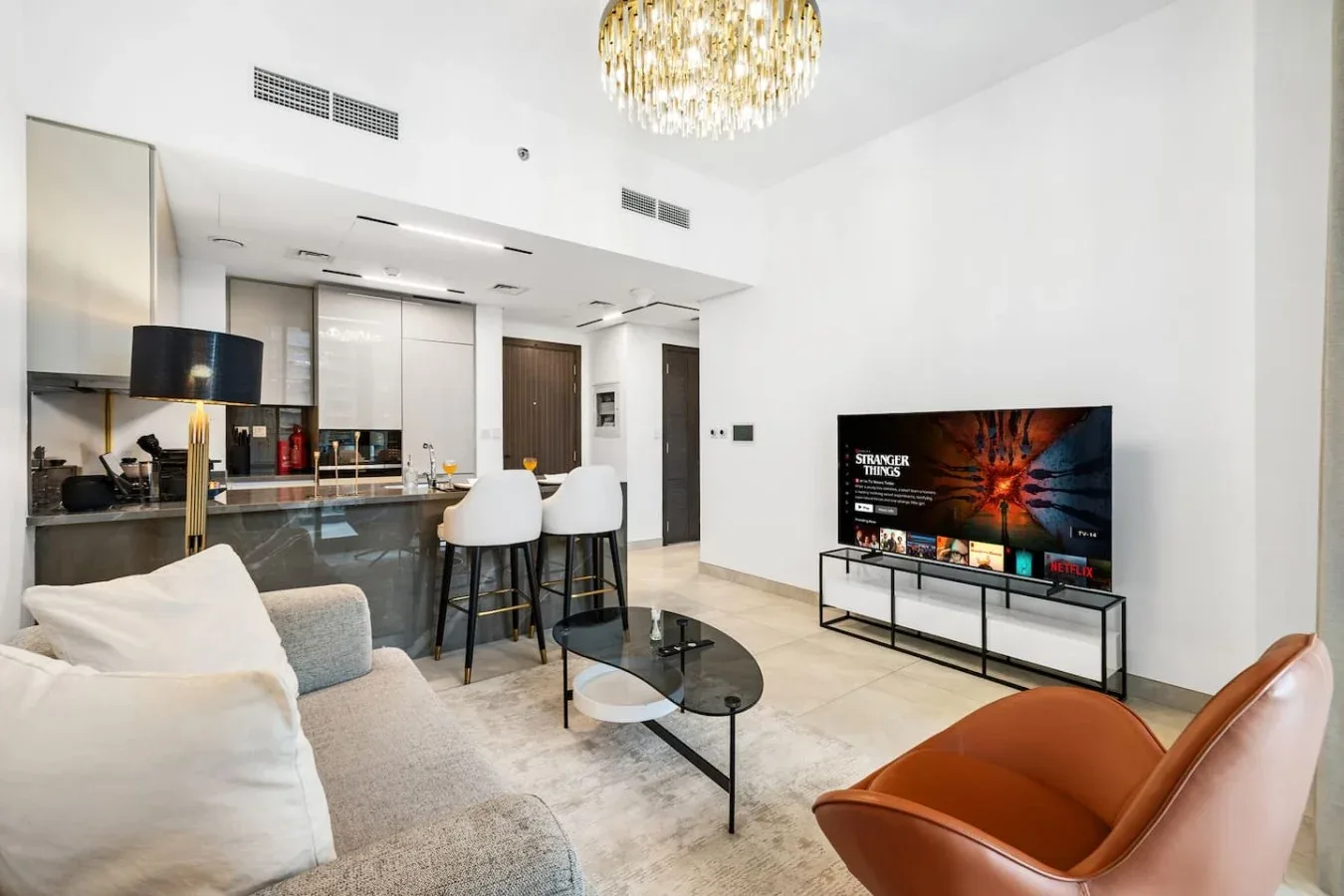 A bright living room with a television, coffee table, and seating beside an open kitchen.