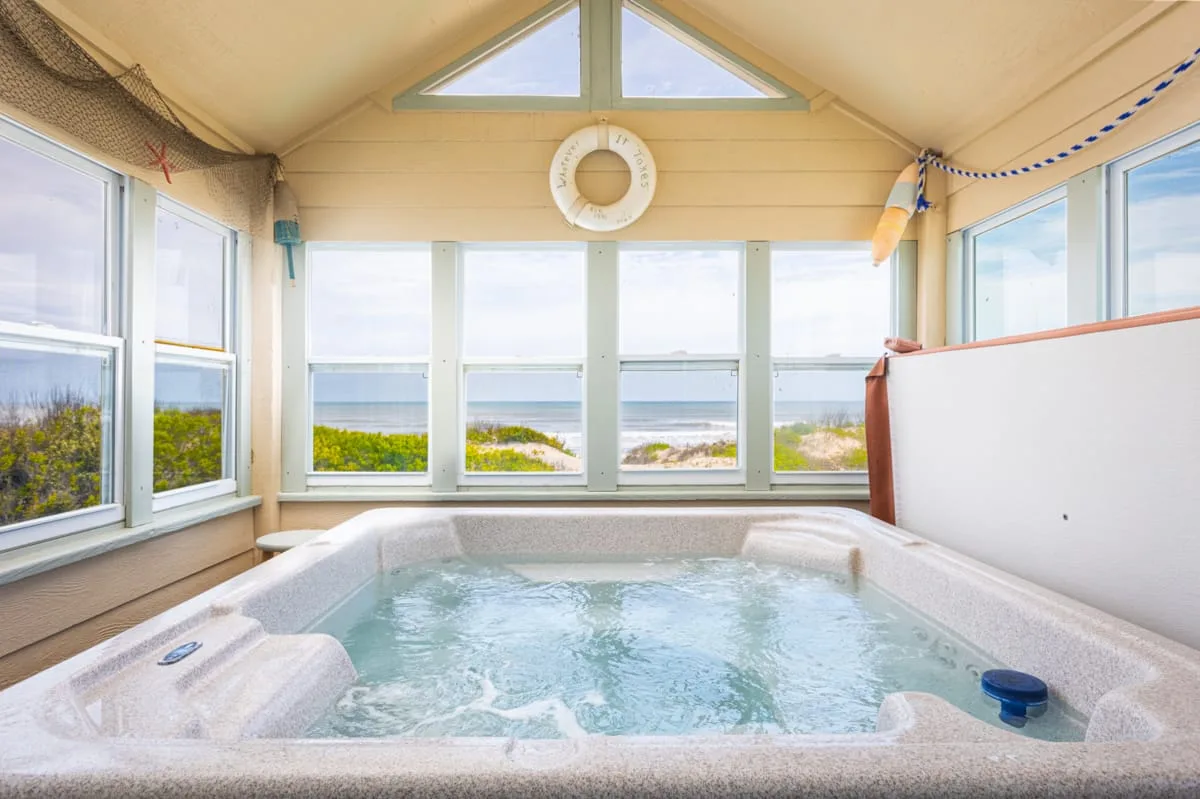 Una luminosa sala con jacuzzi interior y grandes ventanas con vista al océano.