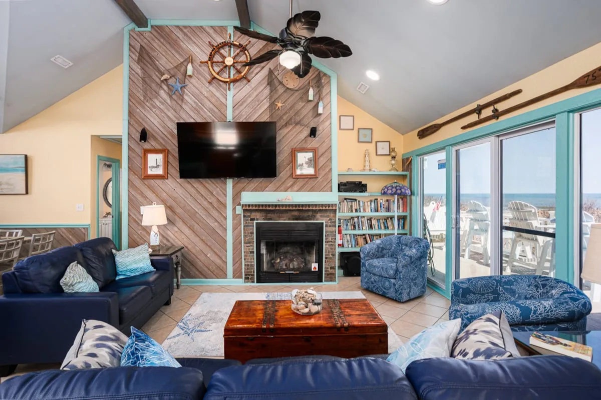 Una sala de estar con asientos azules, una chimenea y grandes ventanales con vistas al agua.